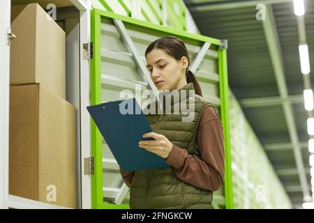 Young woman checking parcel with documents standing in storage Stock Photo