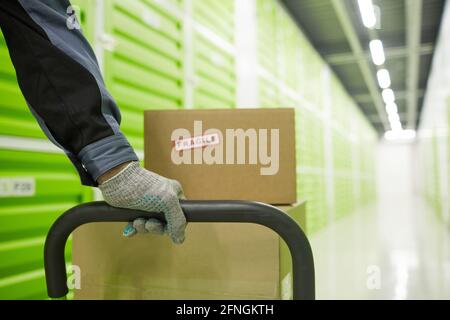 Close-up of man in gloves carrying trolley with parcels in warehouse Stock Photo