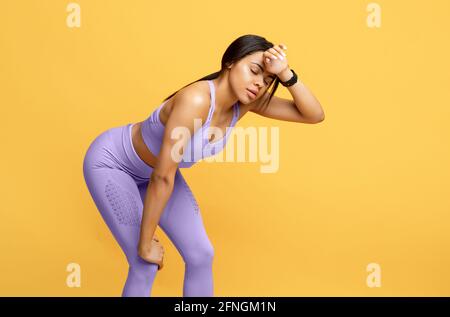 End of race. African american woman in sportswear tired of training and resting on yellow background, free space Stock Photo
