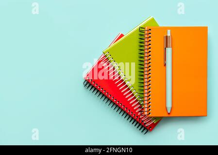top view of colorful spiral notebooks and blue pen with copy space on a blue background.Concept back to school Stock Photo