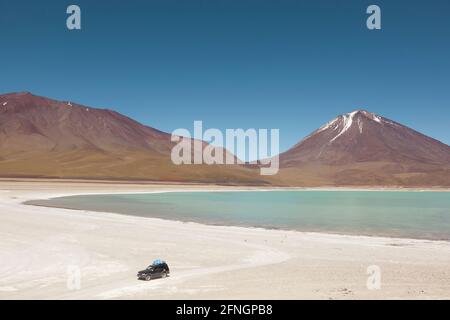 4x4 SUV over-land safari vehicles are seen at the edge of the Laguna Verde in the Bolivian desert. Stock Photo