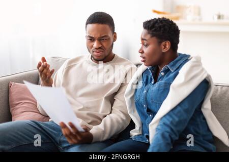Confused black couple reading documentation at home, sitting on couch Stock Photo
