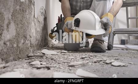 house renovation concept, construction worker holds in hands helmet and safety headphones, he wears the tool bag on his belt , close up with wall plas Stock Photo