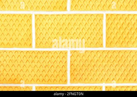 Wall of yellow corrugated brick, brick wall texture, curly neat masonry with a light seam, close-up. Stock Photo
