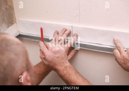 Stylish trendy white ceramic tiles on the kitchen wall. Hands in the process of laying white rectangular tiles on the bathroom wall. Renovation of apa Stock Photo