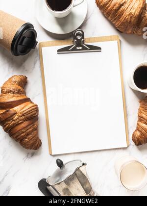 Flat lay frame of cups of coffee, croissants and clipboard with blank sheet for menu entry on marble background. French breakfast concept. Top view. C Stock Photo