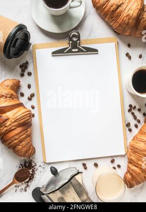 Flat lay frame of cups of coffee, croissants and clipboard with blank sheet for menu entry on marble background. French breakfast concept. Top view. C Stock Photo