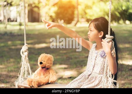 Sad girl feeling alone in the park. Lonely concepts. Beautiful toddler girl and fluffy stay alone under the big tree Stock Photo