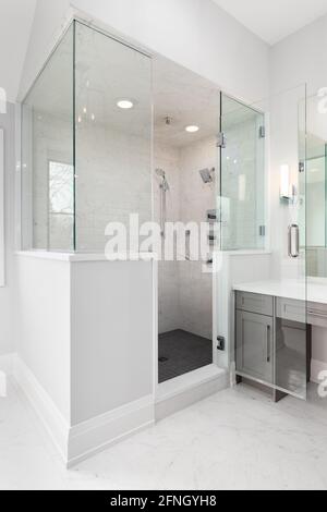 A large walk-in shower in a luxury bathroom that's lined with glass and marble subway tile walls and a dark tiled floor. Stock Photo