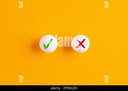 Right versus wrong or voting yes or no concept. Checkmark and cross icons on table tennis balls on yellow background. Stock Photo