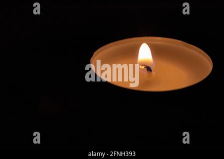 Single lit tealight candle against black background Stock Photo
