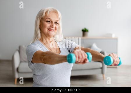 Mature woman exercising at home with two dumbbells Stock Photo