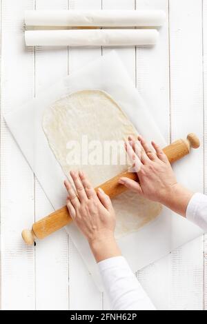 Woman hands spreading a very thin strudel dough with a rolling pin on a sheet of kitchen paper with cornstarch to prevent sticking Stock Photo