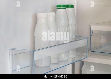 Dairy products in in white plastic bottles on shelf of open empty fridge. White yoghurt in refrigerator. Fermented food. Stock Photo