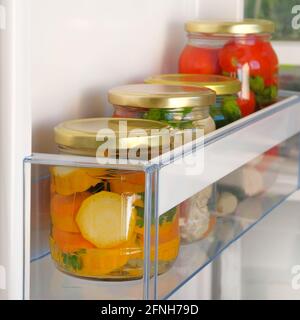 Glass jars with homemade pickled yellow and red vegetables on shelf of refrigerator. Fermented healthy natural vegetarian food concept Stock Photo