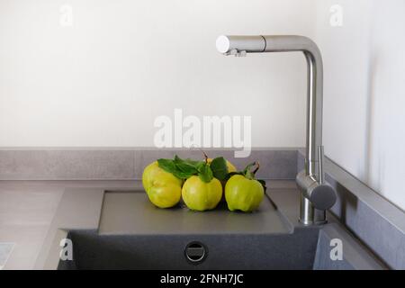 Yellow juicy apple quince next to sink in kitchen room. Modern counter with sink in kitchen room. Washing vegetables concept. Stock Photo