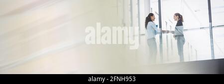 Two caucasian women having an handshake in front of to colleagues Stock Photo