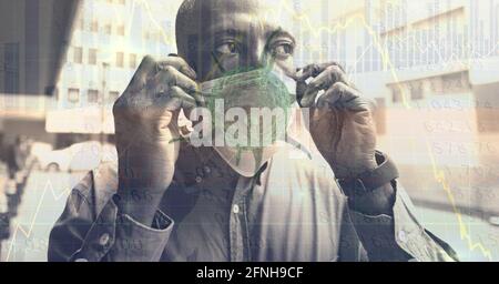 Composition of data processing and covid 19 cell over man wearing face mask in city Stock Photo
