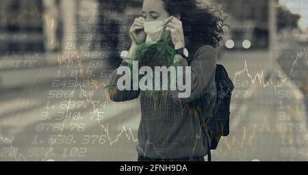 Composition of data processing and covid 19 cell over woman wearing face mask in city Stock Photo