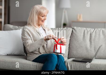 Smiling Mature Woman Holding Present Box Using Laptop Stock Photo