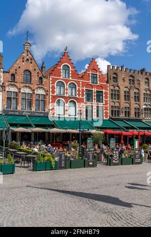 Bruges, Belgium - 12 May, 2021: people enjoy a day out in the restaurants on Market Square in Bruges with many historic brick buildings in the backgro