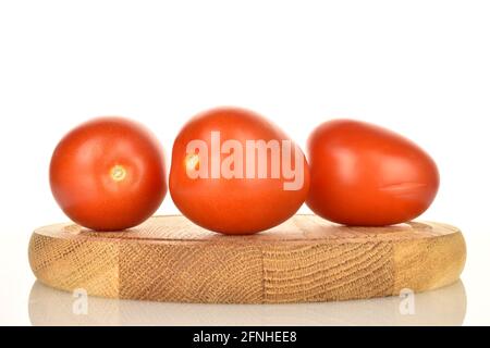 Three bright red organic tomatoes on a round wooden tray, close-up, on a white background. Stock Photo