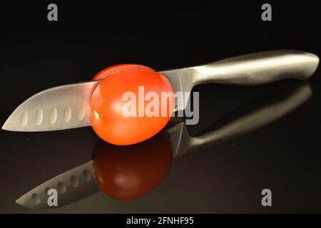 One organic red tomato with a metal knife, close-up, on a black background. Stock Photo