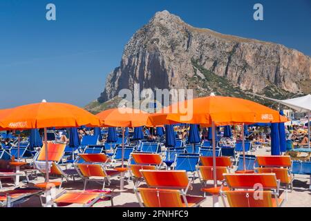 San Vito Lo Capo, Trapani, Sicily, Italy. View along crowded shore to the towering north face of Monte Monaco, striking beach furniture in foreground. Stock Photo