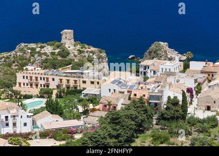 Scopello, Trapani, Sicily, Italy. View over village rooftops to ancient watchtower on cliffs above the deep blue waters of the Gulf of Castellammare. Stock Photo