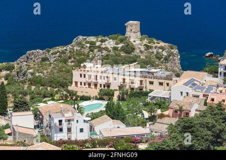 Scopello, Trapani, Sicily, Italy. View over village rooftops to ancient watchtower on cliffs above the deep blue waters of the Gulf of Castellammare. Stock Photo