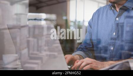 Composition of man using laptop over stacked up shelves with boxes in warehouse Stock Photo