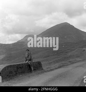 1958,  historical, a lady walker sitting on a low brick bidge wall on a narrow paved road in the Highlands of Scotland. Stock Photo