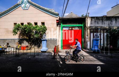 A man cycles past the entrance to Wat Mangkon in the Chinatown area of Bangkok, Thailand Stock Photo