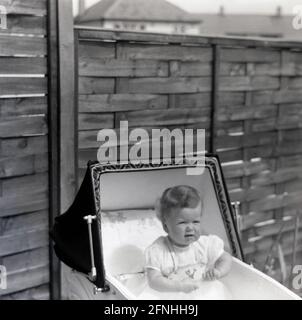1959, historical, outside of a house, an infant girl sitting upright in a coachbuilt pram of the era, England, UK. Stock Photo