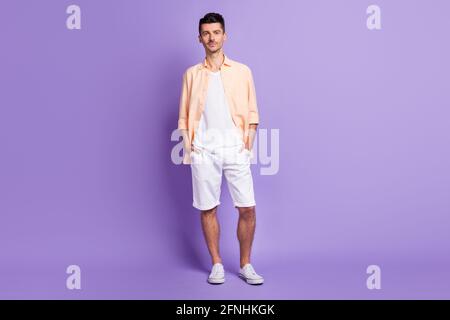 Full size photo of optimistic brunet guy wear peach shirt shorts sneakers isolated on lilac color background Stock Photo