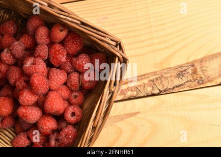 Red organic, ripe raspberry berries in a basket, close-up, on a wooden table, top view. Stock Photo