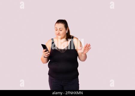 Music Lover. Portrait of overjoyed overweight female model wearing black casual clothes, singing and using wireless earphones and smart phone as mic Stock Photo