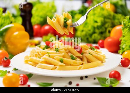 Plate of italian pasta, penne rigate on fork with tomatoes and basil Stock Photo