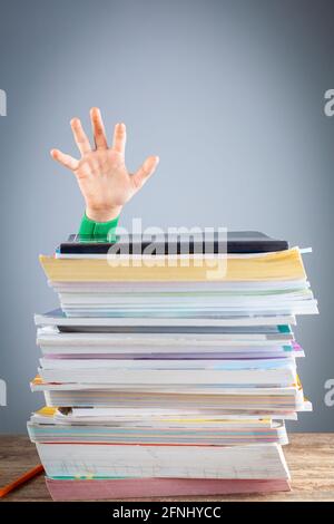 Abstract concept image showing a young student behind a large pile of test prep books on a study desk. An overwhelming load. The kid is trying to rais Stock Photo