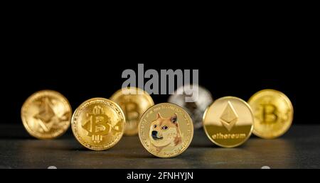 Symbolic cryptocurrency types represented as shiny coins are lined up against dark background. Among them dogecoin which started as a joke is currentl Stock Photo