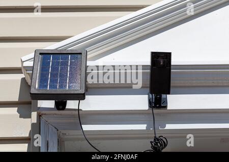 a wireless security surveillence camera with motion sensor on top of the front door frame. The camera is linked to a solar panel for environmental fri Stock Photo