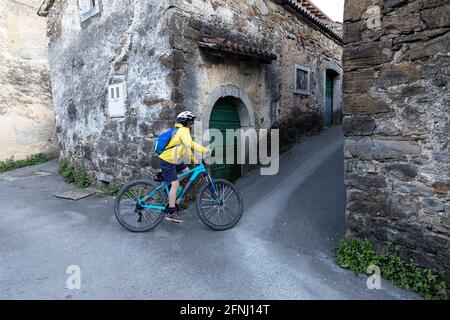 Boy cycling in the narrow street of Goce, little village in the Vipava valley, Slovenian countryside, passing by rustic traditional stone houses,