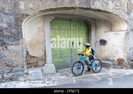 Boy cycling in the narrow street of Goce, little village in the Vipava valley, Slovenian countryside, passing by rustic green door