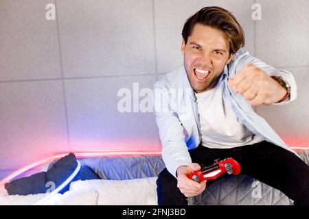 Round one, fight. Excited emotional student, freelancer playing console video games pushing buttons on controller, having fun. Rejoices at success and Stock Photo