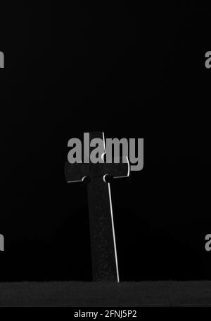 Mono image in portrait format of single stone cross at night against a black background with light highlighting one side and making it stand out Stock Photo