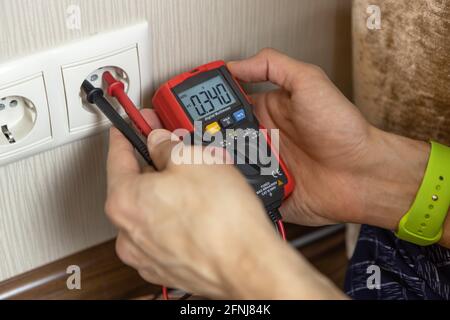 An unrecognizable male technician measures the voltage at the outlet with a digital multimeter. There are only hands in the frame, close-up. Renovatio Stock Photo