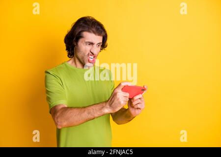 Photo of crazy angry guy hold telephone play videogame look screen wear green t-shirt isolated yellow color background Stock Photo