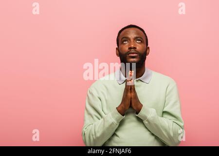 African american man with praying hands looking up isolated on pink Stock Photo
