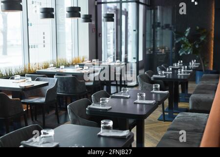 Modern interior of restaurant in gray color furnished soft chairs and black tables with glasses and napkins Stock Photo