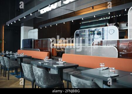 Fashionable cafe with gray furniture and different-shaped panels between zones, wooden planks with lamps above tables Stock Photo